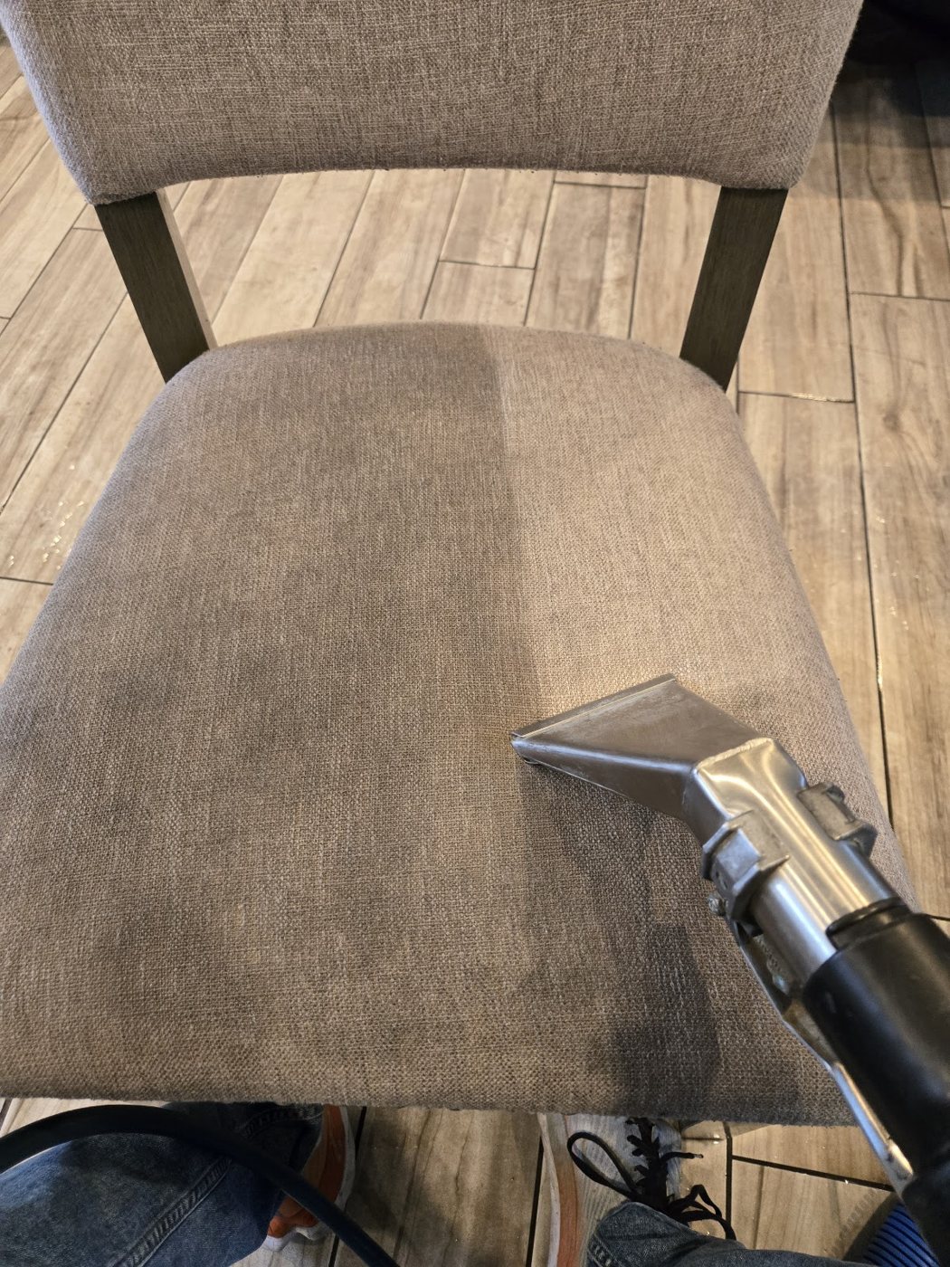A cleaning tool lifting dirt from a gray upholstered dining chair seat
