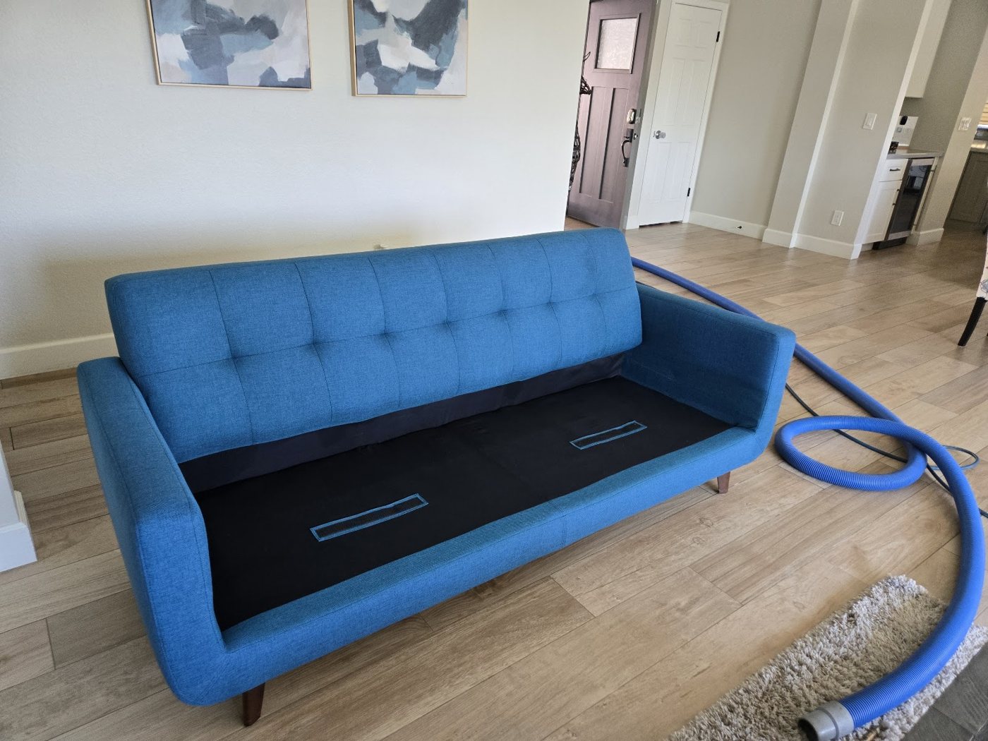 A blue tufted sofa with the cushion base open and a cleaning hose beside it